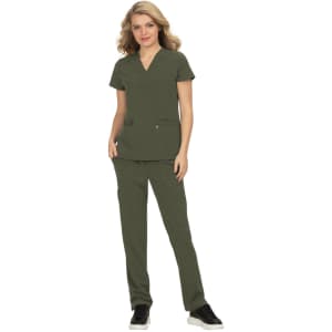 A woman wearing an olive green scrub set with a v-neck top and pants, featuring pockets. The outfit includes a logo.