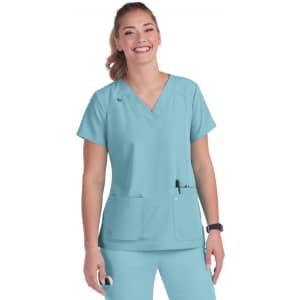 A woman wearing a teal scrub top with a V-neck and two front pockets, smiling at the camera.