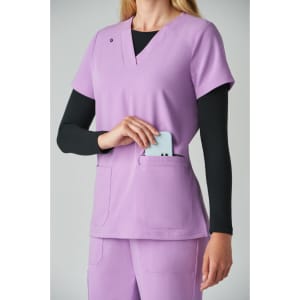 A lavender top featuring a V-neck design and pocket, worn over a long-sleeve black shirt. It has a branding logo.
