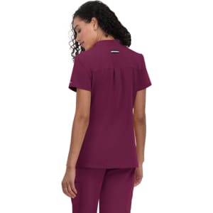 A woman wearing a maroon medical scrub top with short sleeves and a back pleat. The top features a small logo.