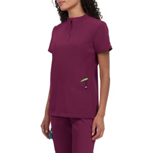 A maroon medical scrub top with a short collar and two front pockets. It has a logo on the sleeve.