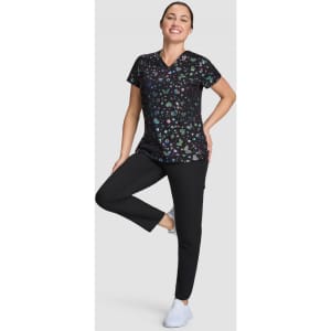 A woman is wearing a black patterned top with various colours, paired with black pants and white shoes.