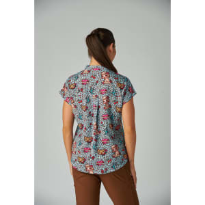 A short-sleeved, patterned women's top in blue with vibrant colours and a playful design. It features a collar and has a logo.