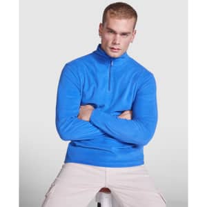 A blue polar fleece jumper with a half zip, featuring a logo, modelled by a seated male figure.