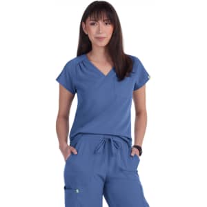 A blue scrub top with a V-neck and a pocket, worn by a model. The top features short sleeves and a relaxed fit.