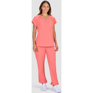 A woman is wearing a coral top and matching pants, featuring a pocket and a logo. The outfit is styled for comfort.