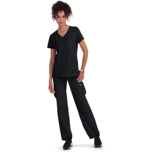 A woman wearing a black scrubs outfit, featuring a short-sleeve top and cargo pants, standing with hands on her hips.