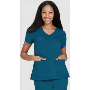 A teal scrub top featuring short sleeves and two front pockets, modelled by a smiling woman.