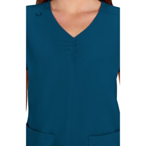 A teal medical scrub top featuring a V-neck design and gathered detailing at the front. It has pockets and a logo.