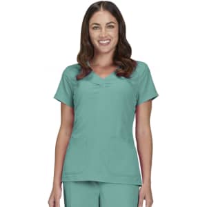 A scrub top in teal featuring short sleeves and two front pockets. The model smiles while wearing the top.