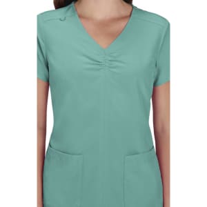 A scrub top in a teal colour with a V-neck and short sleeves, featuring two front pockets and a logo.