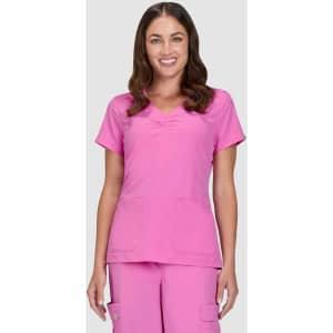 A pink scrubs top featuring a V-neck design and two front pockets, modelled by a smiling woman.