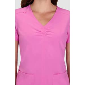A pink scrub top featuring a V-neck and ruched detailing, with pockets at the front and a brand logo.