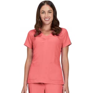 A woman wearing a coral scrub top with a scoop neckline and two front pockets.
