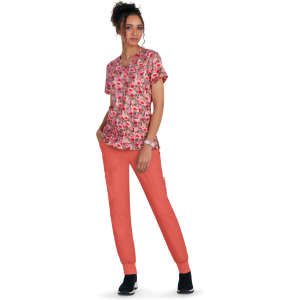 A woman in a floral pink top and coral jogger pants stands against a white background. The outfit features a logo.