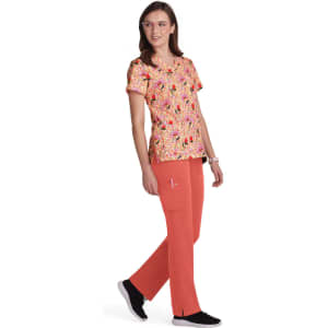 A woman wearing a colourful floral print top in shades of pink and orange, paired with coral pants and black shoes.