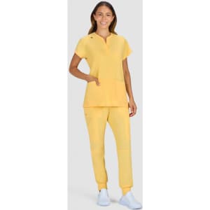 A model in a bright yellow top and matching pants, featuring pockets and a logo. The outfit is paired with white shoes.