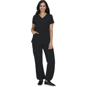 A woman wearing a black scrub top and black pants, standing with one hand in her pocket. The outfit includes a logo.