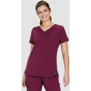A maroon Sari Top featuring a V-neck and two front pockets, worn by a smiling model. The top has a brand logo.