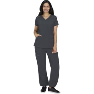 A woman wearing a charcoal grey medical scrubs set, featuring a V-neck top and matching pants, stands smiling.