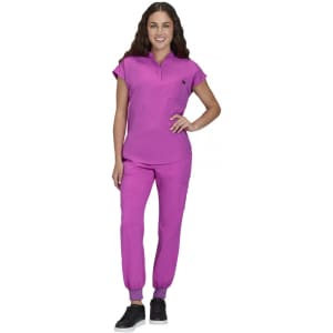A woman stands in a vibrant purple outfit, comprising a short-sleeved top and fitted pants. The outfit has a small pocket and a logo.