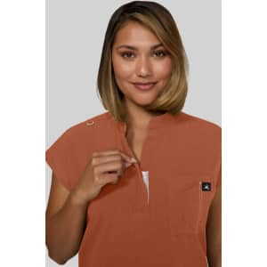 A woman with shoulder-length hair models an orange top with a zippered neckline and a logo.