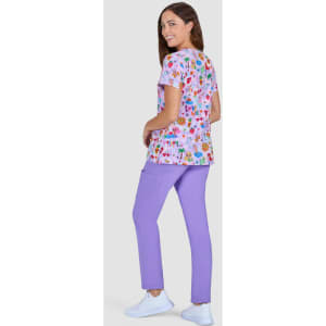 A woman wearing a floral print top in pink and purple, paired with lilac pants and white shoes, standing against a grey background.