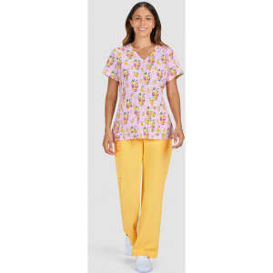 A woman wears a pink patterned top featuring floral designs and yellow trousers, posing against a grey background.