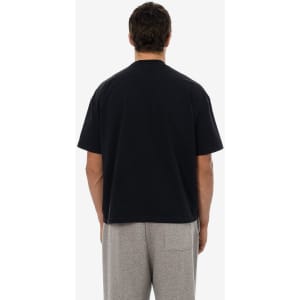 A short sleeve black garment dye t-shirt viewed from the back, worn with grey trousers. The shirt features a logo.