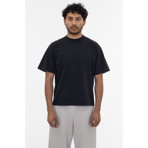 A black short sleeve garment dye t-shirt worn by a person, paired with light grey pants, featuring a logo.