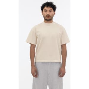 A short sleeve garment dye t-shirt in a beige colour, worn by a model with curly hair and grey pants.