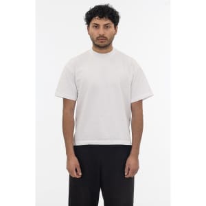 A short sleeve garment dye t-shirt in a light colour, featuring a logo, worn by a model standing against a plain background.
