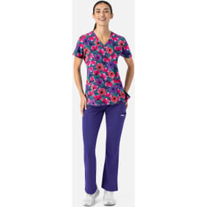 A woman wearing a colourful floral V-neck print top with purple pants, smiling and standing confidently.