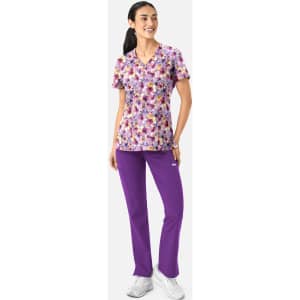 A woman wearing a floral v-neck print top in purple and pink, paired with purple pants. The outfit includes a logo.