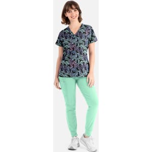 A woman wearing a black v-neck top with a colourful print, paired with mint green pants and white shoes.