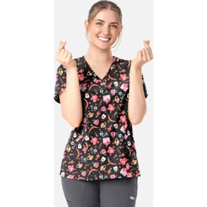 A woman in a black V-neck print top featuring a colourful pattern of hearts and various designs, smiling and gesturing with her hands.