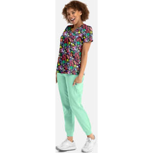 A woman poses in a vibrant floral print V-neck top with short sleeves, paired with mint green joggers.