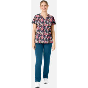 A floral print women's V-neck top in vibrant colours, paired with teal pants and worn with white shoes.