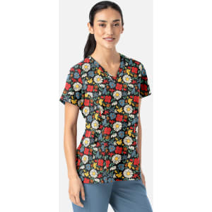 A woman wears a floral V-neck top featuring red, yellow, and white flowers on a dark background. The top has a logo.
