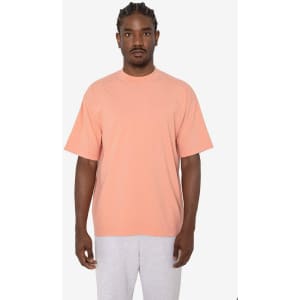 A short sleeve crewneck tee in a soft peach colour, featuring a relaxed fit and a branding logo.
