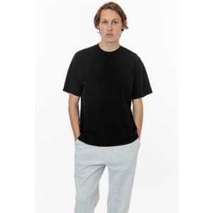 A black short sleeve crewneck t-shirt worn by a model, paired with light grey pants. The t-shirt features a logo.