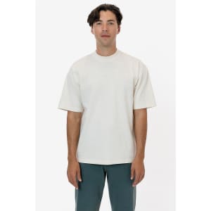 A man wearing a short sleeve, garment-dyed crewneck tee in a light beige colour, standing against a white background.