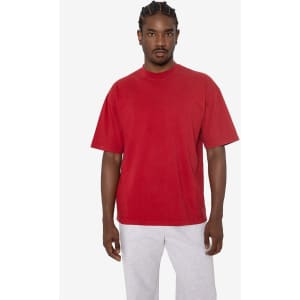 A short sleeve crewneck tee in red, featuring a relaxed fit and a logo. Model is wearing grey pants.