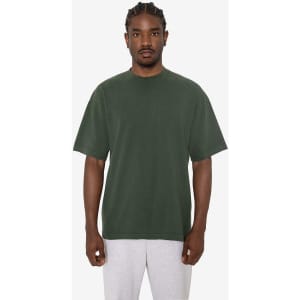 A green short sleeve crewneck tee with a loose fit, featuring a logo. Model wearing grey sweatpants.