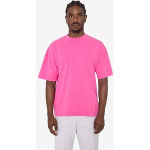 A pink short sleeve crewneck tee worn by a model, paired with grey sweatpants. The tee features a logo.