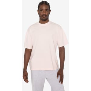 A short sleeve crewneck t-shirt in a soft pink colour, worn by a model with braided hair. Features a logo.
