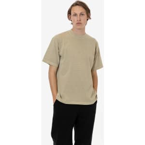 A short sleeve garment dye crewneck tee in a muted beige colour, worn by a model with hands in pockets.