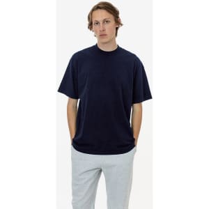 A short sleeve crewneck tee in navy, worn by a model with hands in pockets, paired with grey pants.