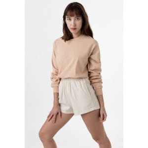 A long sleeve crewneck tee in peach, paired with light beige shorts, displayed on a model against a neutral backdrop.