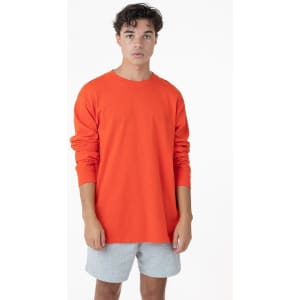 A model wearing an orange long sleeve crewneck tee paired with grey shorts, standing against a plain background.